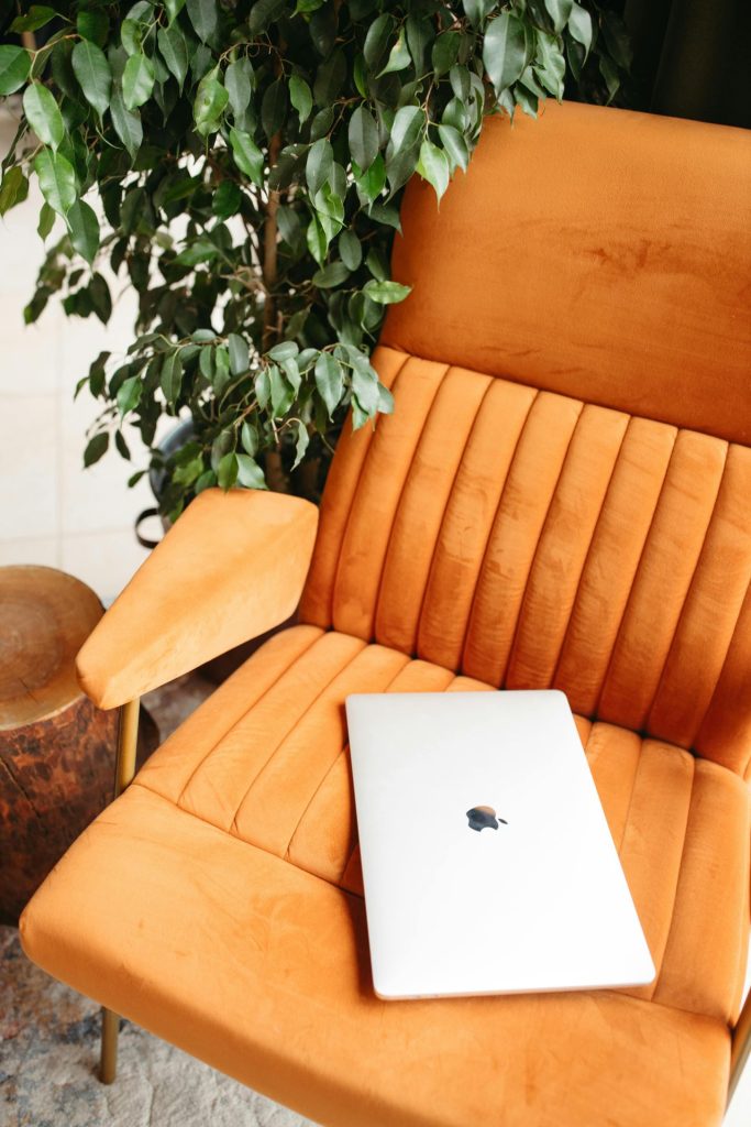 Ordinateur portable posé sur un fauteuil orange à côté d'une plante verte.