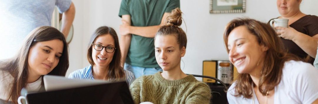 Groupe de personnes collaborant autour d’un ordinateur portable, tasses de café à la main, dans une ambiance conviviale et professionnelle.